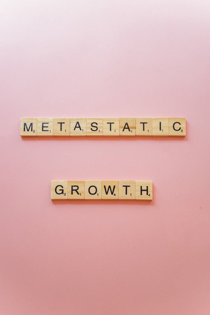 Wooden Scrabble tiles on pink background spelling Metastatic Growth.