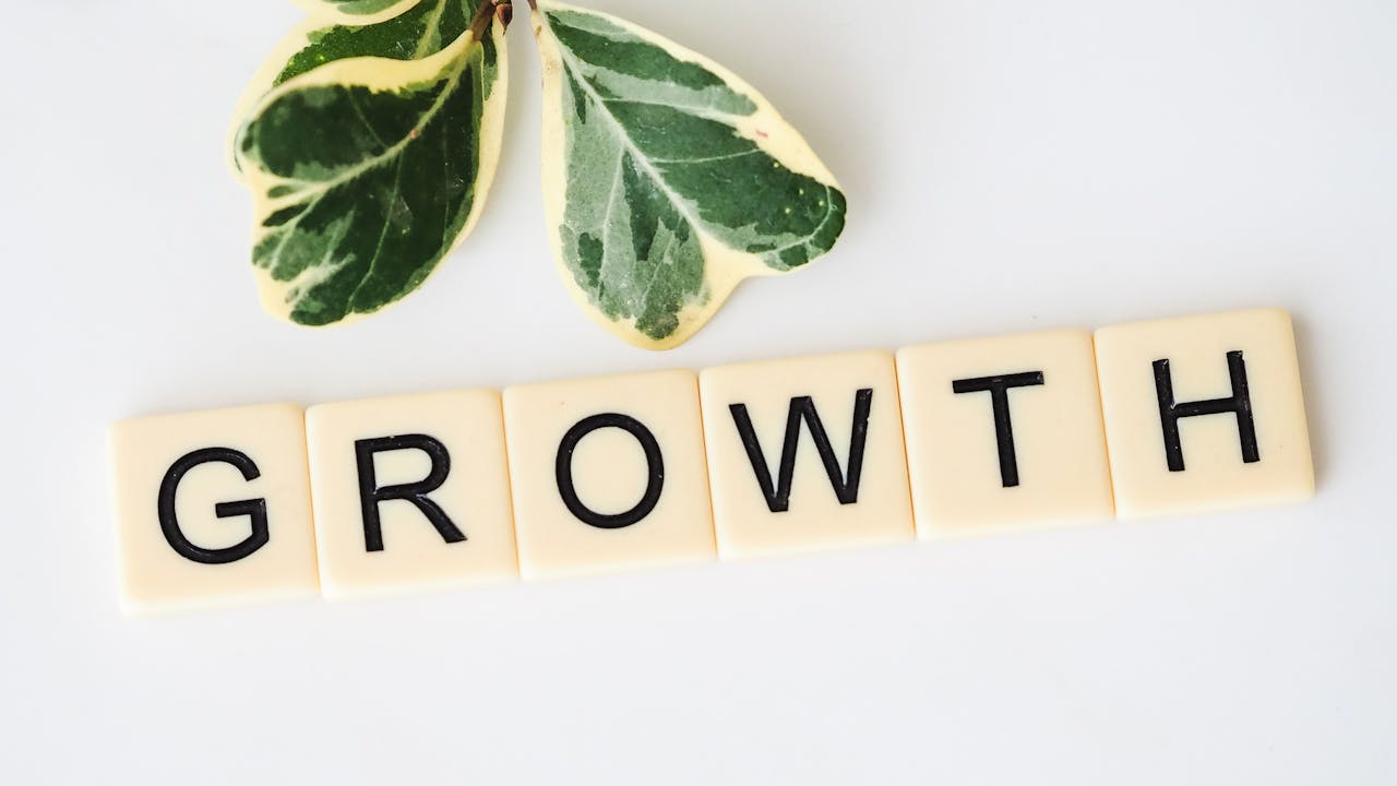 Close-up image of Scrabble tiles spelling Growth with green leaves on a white background.